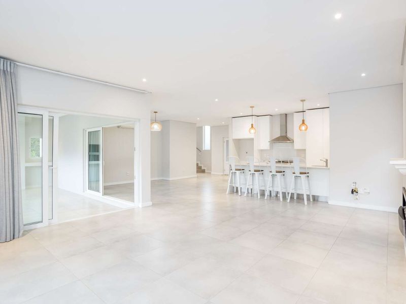 Spacious open-plan living area featuring large format floor tiles, modern kitchen with island, and seamless access to an adjoining patio through sliding glass doors.