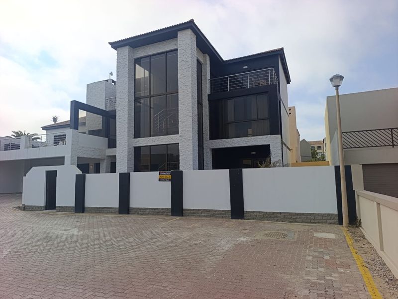 Modern multi-story residential property featuring stone cladding, expansive glass windows, and a private balcony, set behind a secure boundary wall.