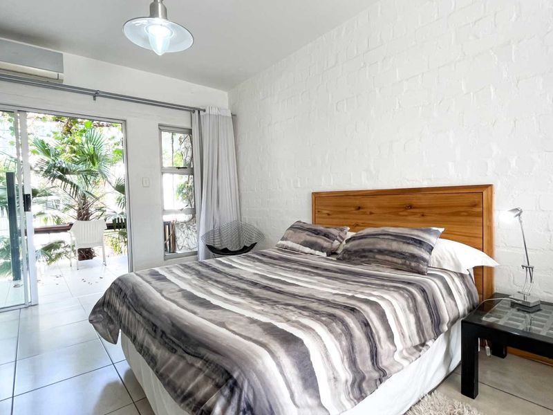 A bright bedroom featuring white painted brick walls, tiled flooring, and a sliding glass door providing direct access to an outdoor patio area.