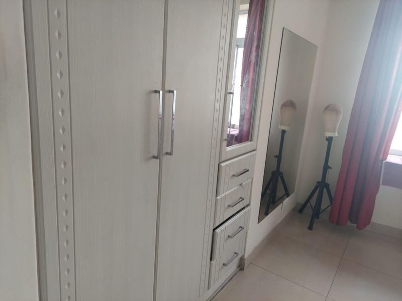 A bedroom featuring a white built-in wardrobe with integrated drawers and a full-length wall mirror, complemented by neutral floor tiles.
