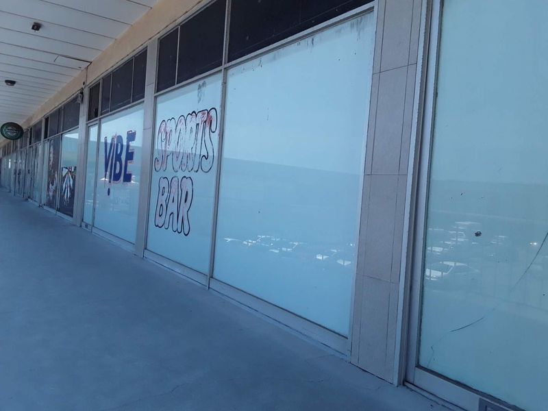 Exterior view of a commercial storefront featuring large glass display windows with signage, located along a covered walkway.