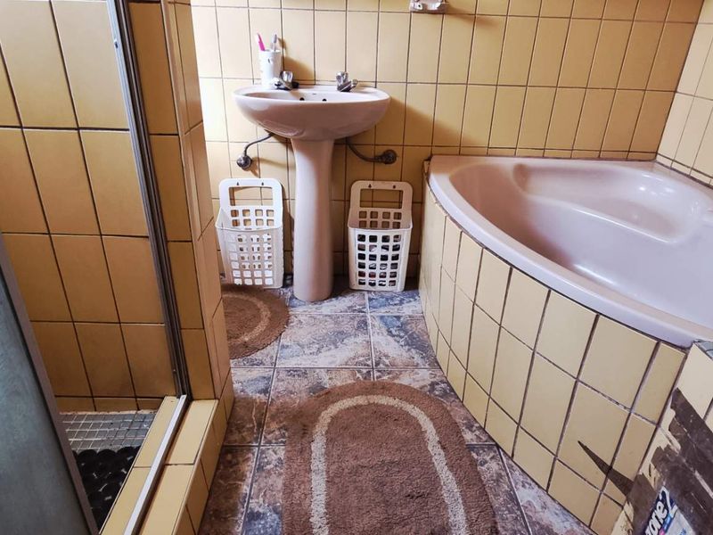 A dated bathroom featuring a corner bathtub, pedestal basin, and separate shower enclosure with yellow ceramic wall tiles and patterned floor tiles.