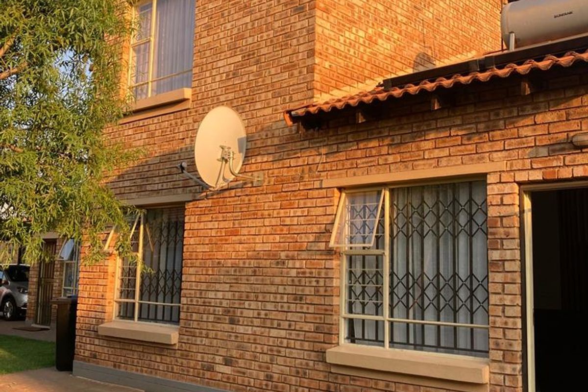 A two-story face-brick townhouse exterior featuring tiled roofing, security bars on windows, and a solar geyser installation.