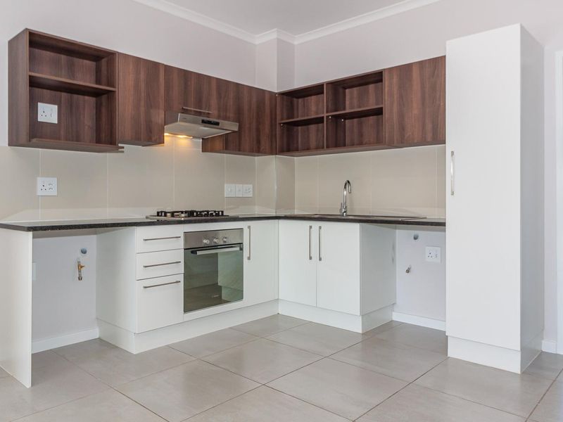 Modern kitchen featuring dark wood upper cabinets, white lower cabinetry, gas hob, electric oven, and tiled flooring with dedicated appliance plumbing connections.