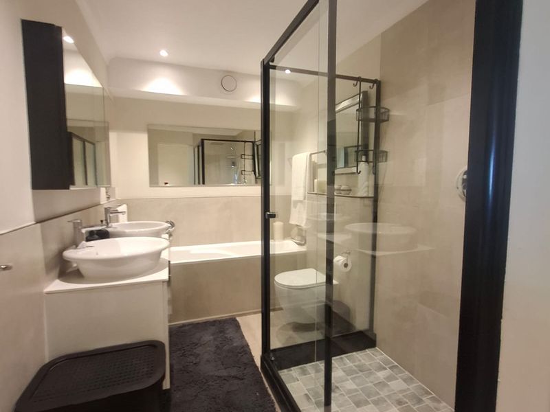 Modern bathroom featuring a double vanity, built-in bathtub, and a spacious walk-in shower with a sleek black frame.