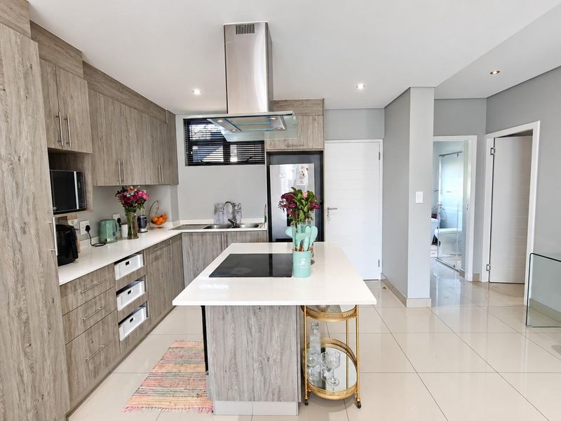 Modern kitchen featuring wood-grain cabinetry, quartz countertops, a central island with an induction cooktop, and high-quality stainless steel appliances.
