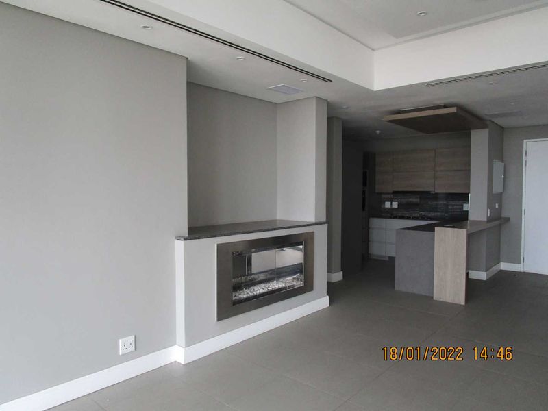 Modern open-plan living area featuring a sleek built-in fireplace, recessed ceiling lighting, and a contemporary kitchen with stone countertops and integrated cabinetry.