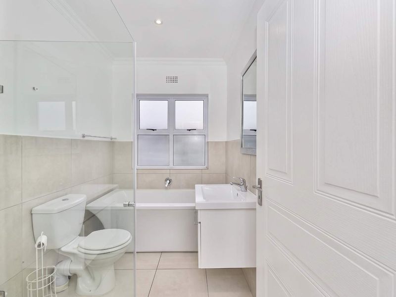 A clean, modern bathroom featuring a built-in bathtub, a vanity basin, and a glass-enclosed shower area with neutral tiled finishes.