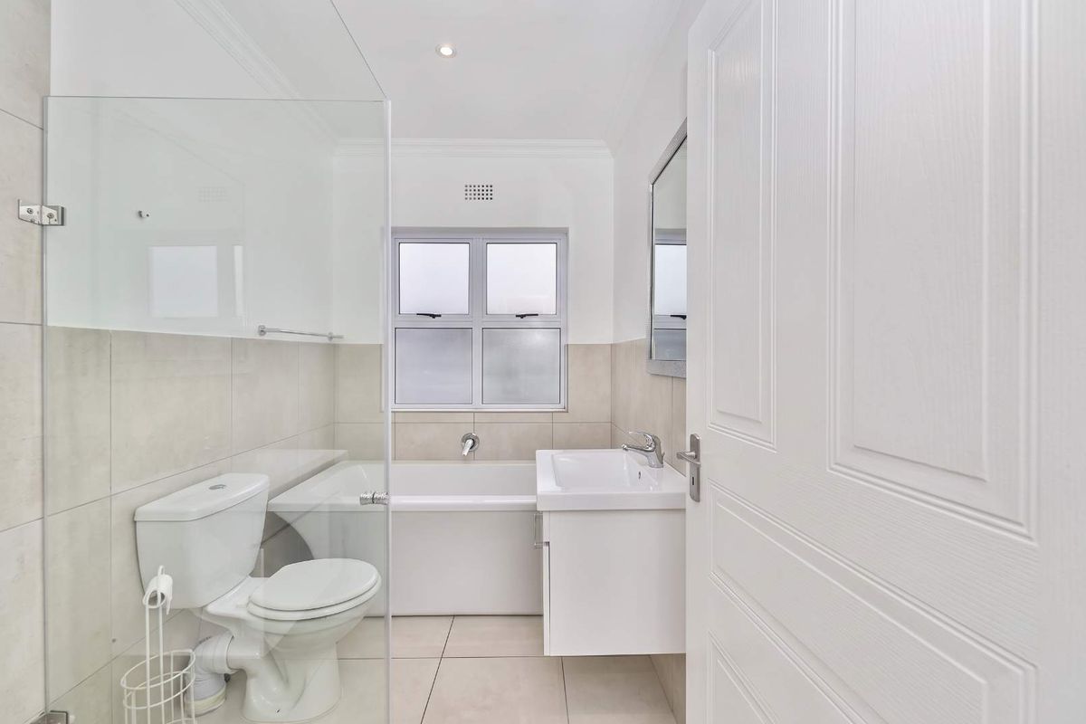 A clean, modern bathroom featuring a built-in bathtub, a vanity basin, and a glass-enclosed shower area with neutral tiled finishes.