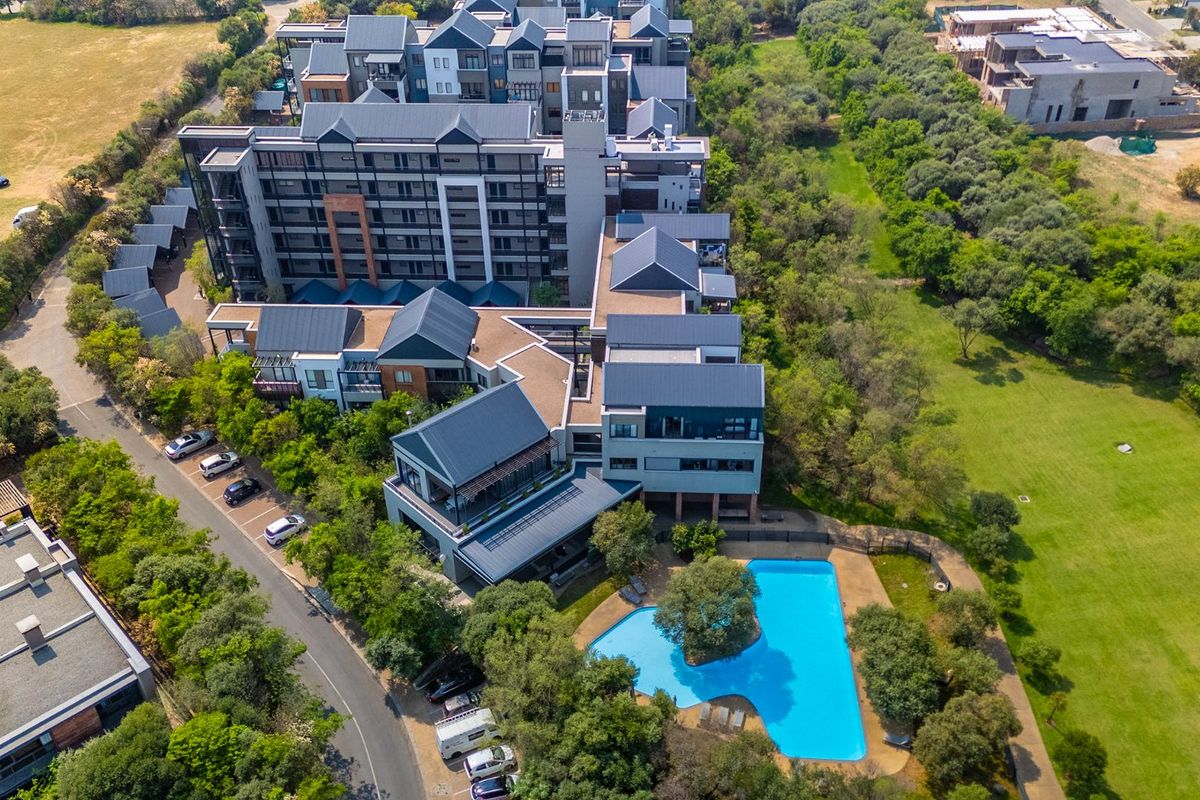 Aerial view of a modern apartment complex featuring a swimming pool, landscaped surroundings, and dedicated parking areas.