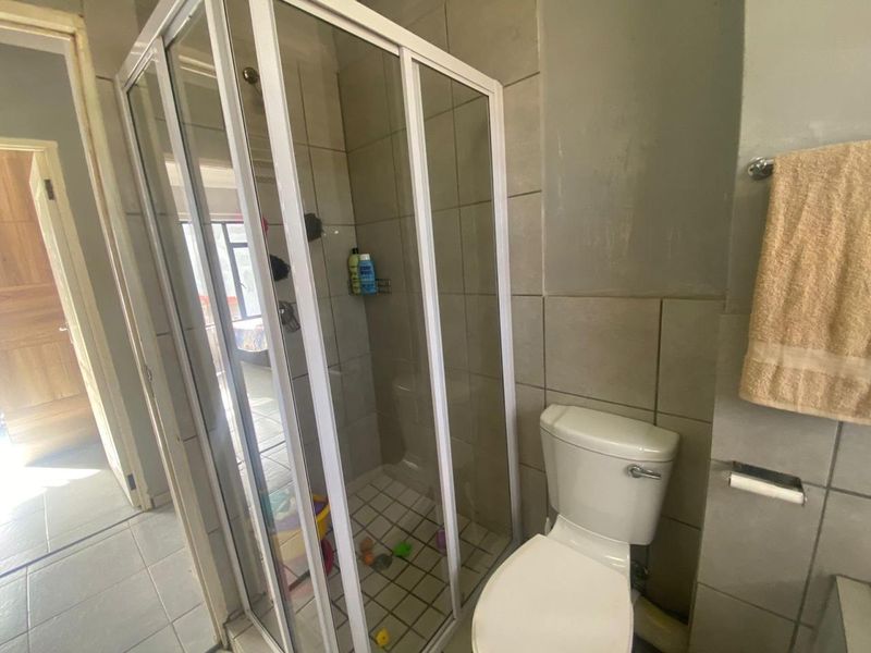 A functional bathroom featuring a corner shower enclosure, a standard toilet, and neutral ceramic wall tiling.