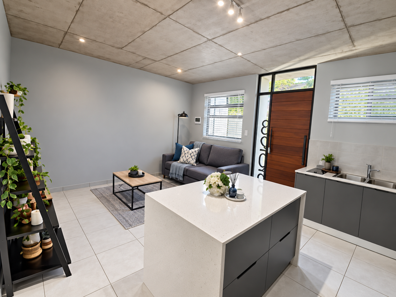 Modern open-plan living area featuring an exposed concrete ceiling, tiled floors, and a sleek kitchen island with quartz countertops and integrated cabinetry.