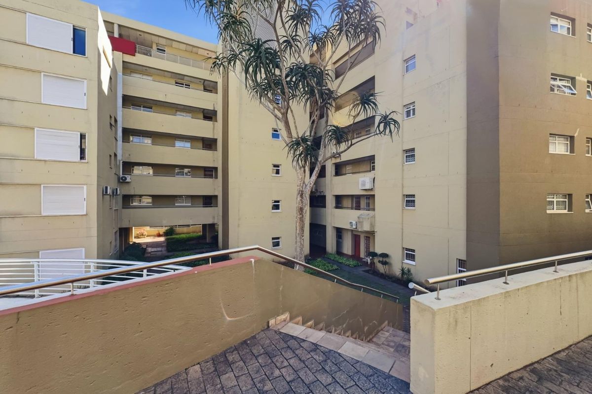View of the apartment complex exterior, featuring a paved staircase, metal handrails, and multiple levels of balconies with external air conditioning units.
