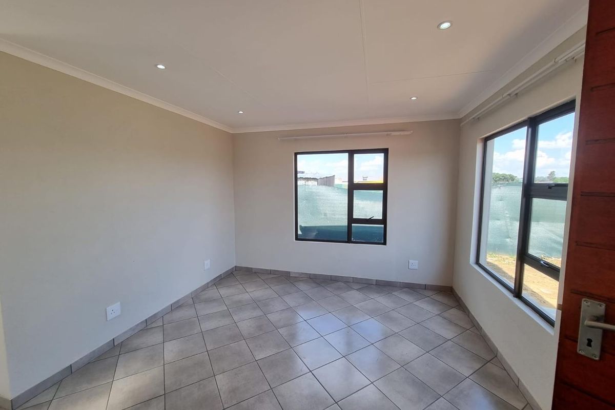 A bright, empty bedroom featuring neutral wall paint, tiled flooring, and modern aluminium-framed windows with recessed ceiling downlights.