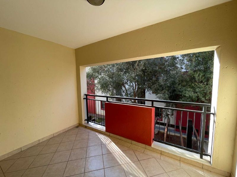A covered balcony featuring tiled flooring and a metal balustrade, offering an open outdoor space with views of surrounding trees.