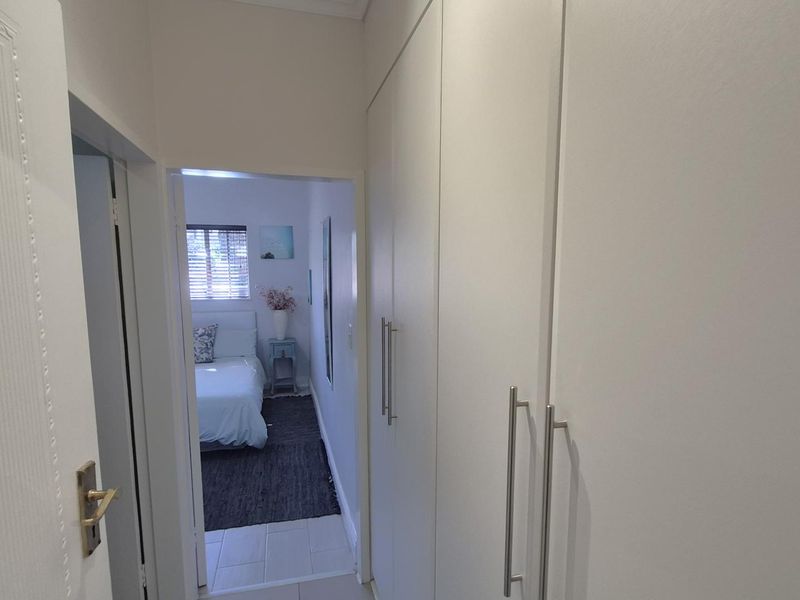 A clean, well-maintained hallway featuring floor-to-ceiling built-in cupboards with modern handles, leading into a bedroom.