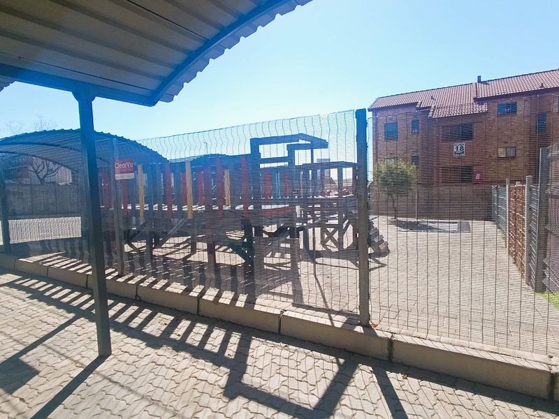 Outdoor communal area featuring paved ground, metal mesh fencing, and a covered parking structure within the apartment complex grounds.