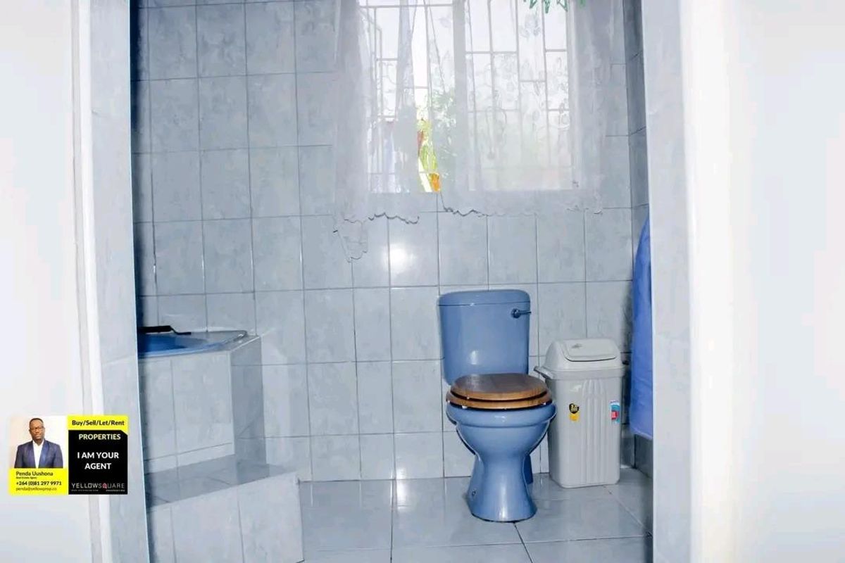 A compact bathroom featuring blue sanitary ware, tiled walls and flooring, and a window with security bars.