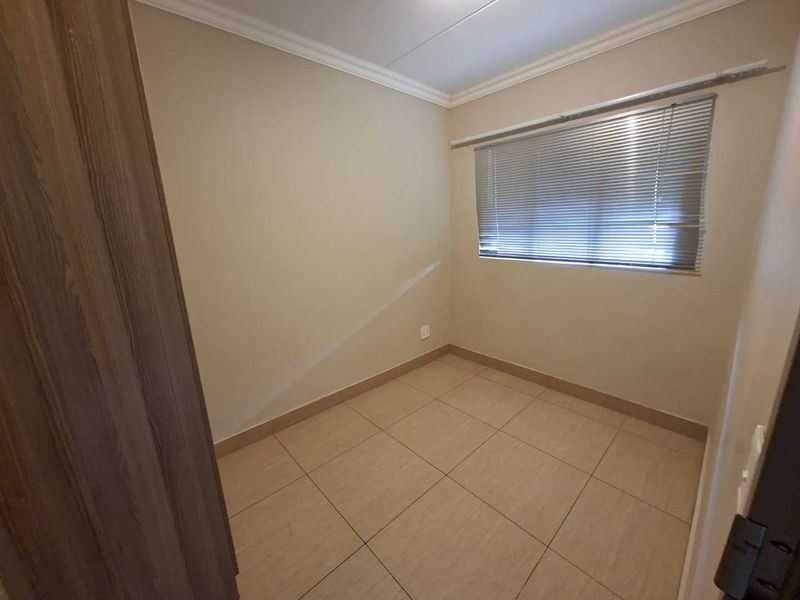 A clean, empty bedroom featuring neutral tiled flooring, a built-in cupboard, and venetian blinds on the window.