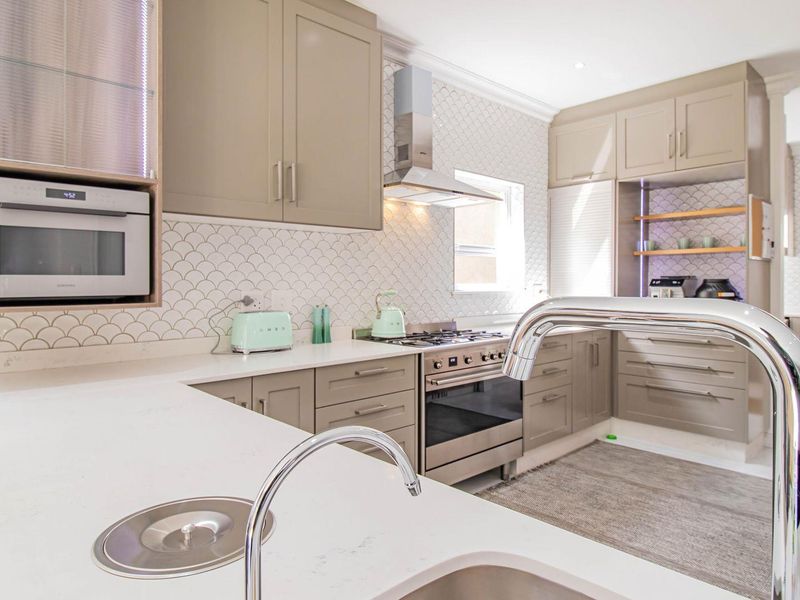 Modern kitchen featuring taupe cabinetry, quartz countertops, a stylish scalloped tile backsplash, and high-quality built-in appliances including a gas stove and microwave.