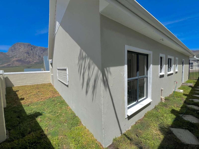 Rear exterior view of the property featuring plastered walls, aluminium window frames with security bars, and a small garden area with mountain views.
