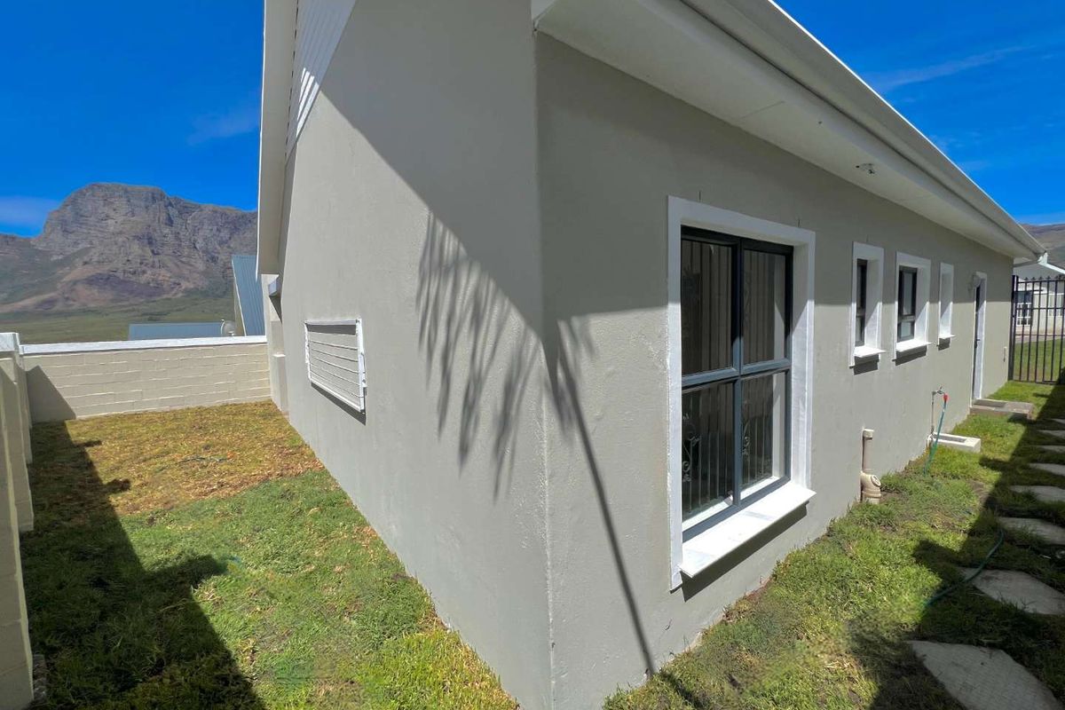 Rear exterior view of the property featuring plastered walls, aluminium window frames with security bars, and a small garden area with mountain views.