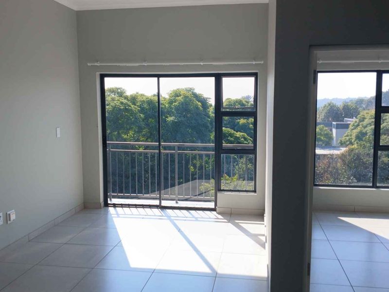 Bright and spacious living area featuring neutral tiled flooring, large sliding glass doors leading to a balcony, and expansive windows with natural light.