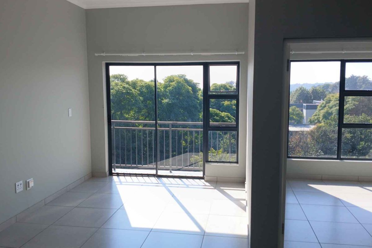 Bright and spacious living area featuring neutral tiled flooring, large sliding glass doors leading to a balcony, and expansive windows with natural light.