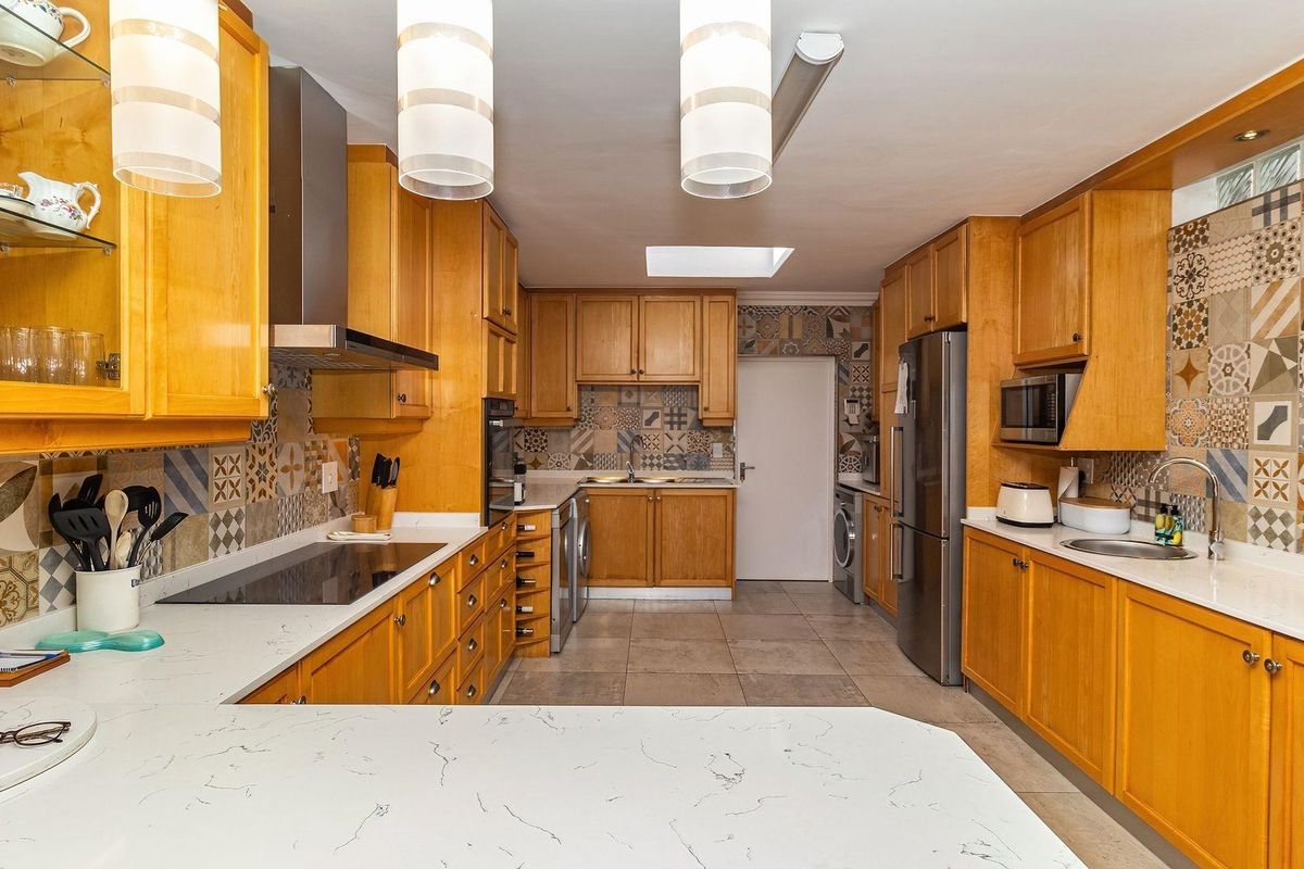 Spacious kitchen featuring warm wooden cabinetry, stone countertops, decorative tiled backsplashes, modern appliances, and a skylight for natural illumination.
