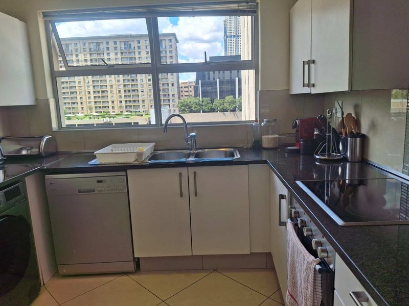 A functional kitchen featuring granite countertops, built-in cabinetry, an electric hob, and a double sink with a view of the surrounding urban area.