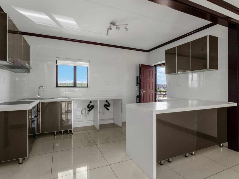 A modern, empty kitchen featuring high-gloss cabinetry, stone countertops, integrated hob, and tiled flooring, offering a clean and functional space ready for customization.