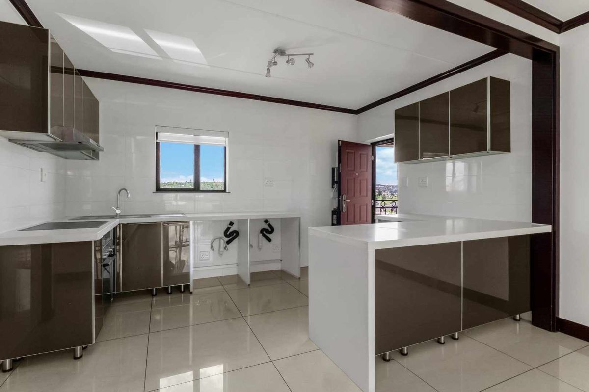A modern, empty kitchen featuring high-gloss cabinetry, stone countertops, integrated hob, and tiled flooring, offering a clean and functional space ready for customization.