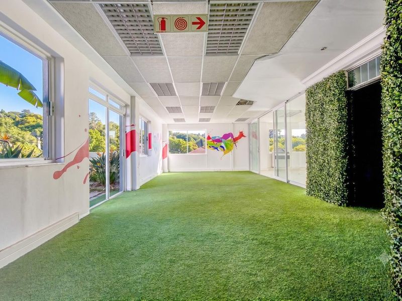 Bright, open-plan office space featuring artificial grass flooring, large sliding glass doors, and a decorative vertical garden wall.