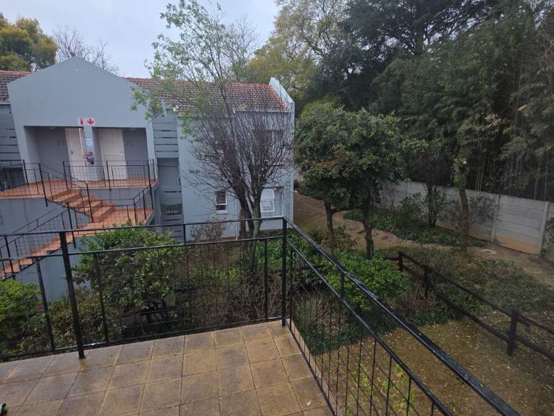 A private balcony featuring tiled flooring and a metal balustrade, overlooking a shared garden area and adjacent apartment building.