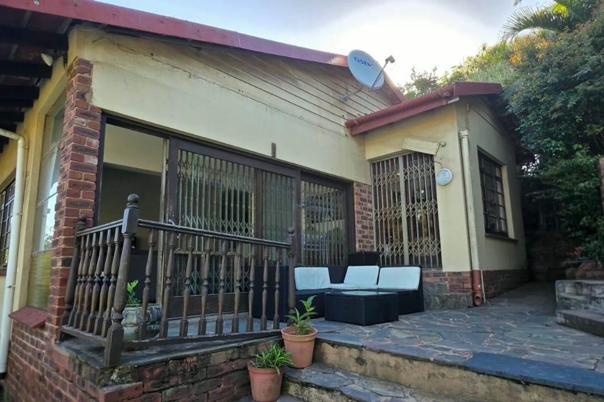 Rear exterior view featuring a stone paved patio, brick built-in braai, and sliding glass doors with security gates.