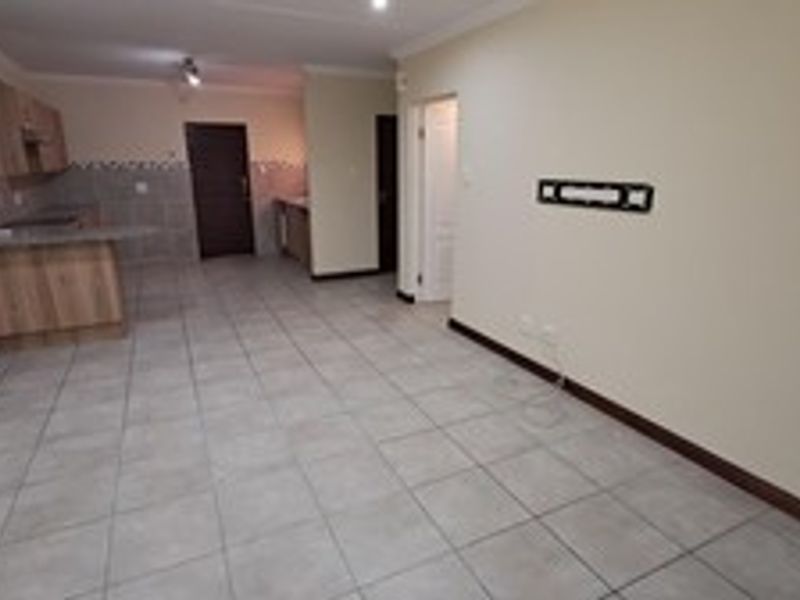 An open-plan living and kitchen area featuring neutral tiled flooring, built-in cabinetry, and a breakfast bar, offering a versatile and functional living space.