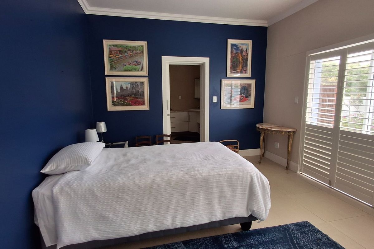 A well-maintained bedroom featuring dark blue accent walls, tiled flooring, and white plantation shutters providing natural light and access to the exterior.
