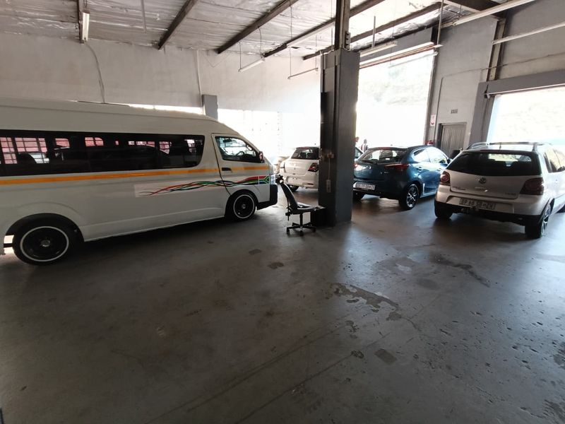 Spacious industrial garage area featuring exposed steel roof trusses, concrete flooring, and a large roller shutter door for vehicle access.