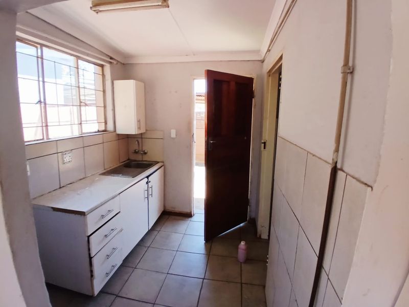 A compact, functional kitchen featuring built-in cabinetry, a stainless steel sink, tiled splashbacks, and direct access to an exterior area.