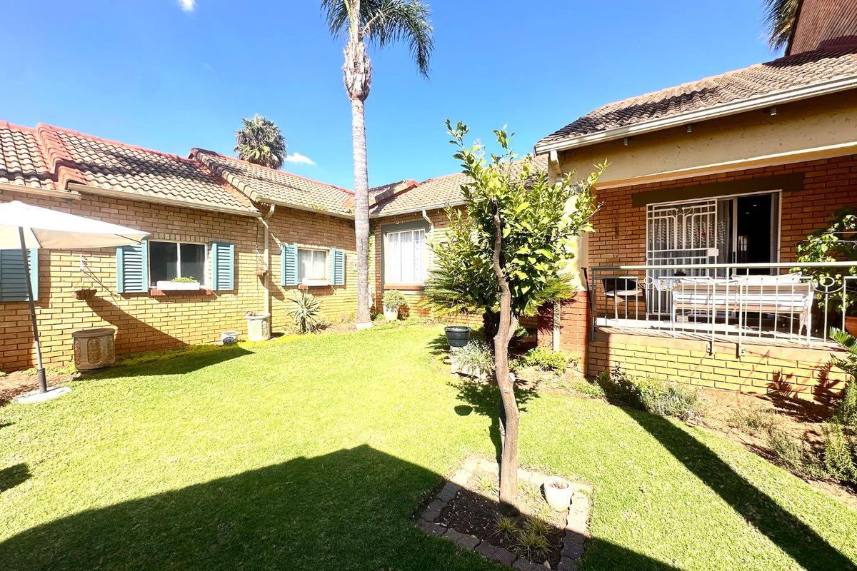 A private rear garden area featuring a brick townhouse facade, a small patio with security gate, and a well-maintained lawn.