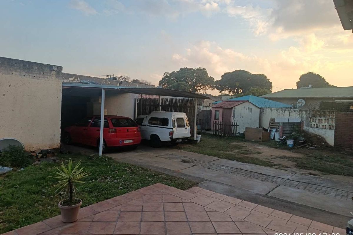Exterior view of the property featuring a paved patio, a covered carport area, and a rear yard with a small storage shed.