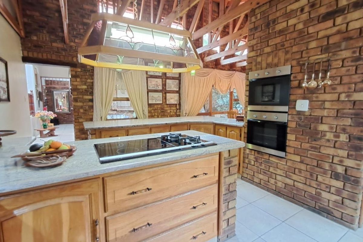 Spacious kitchen featuring exposed brick walls, vaulted timber ceiling, central island with integrated hob, and built-in double oven.
