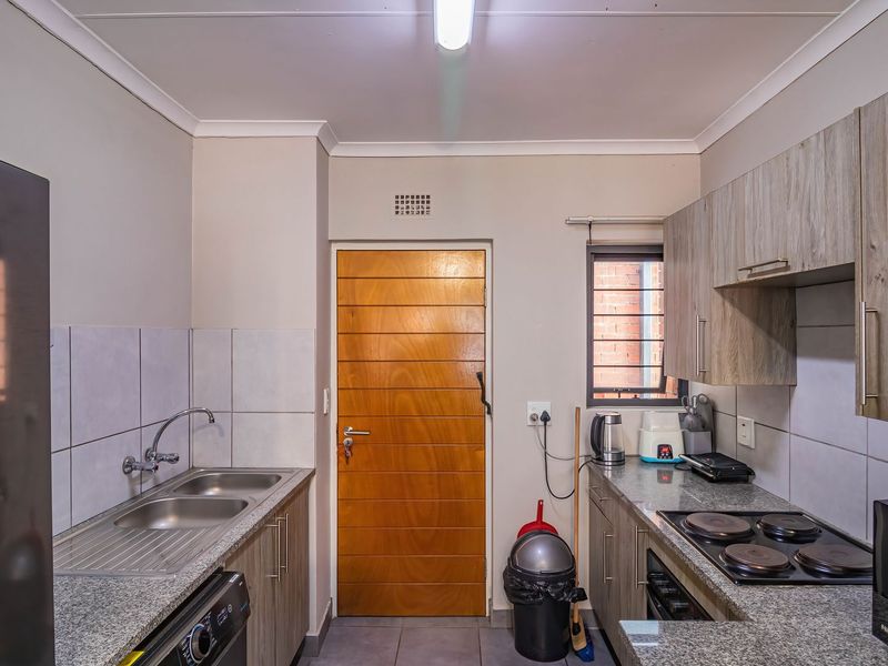 A functional kitchen featuring granite countertops, built-in cabinetry, a double bowl stainless steel sink, and an electric hob with tiled backsplash.