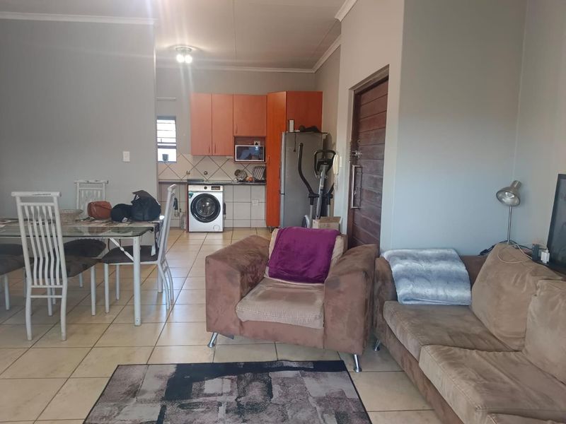 Open-plan living and dining area featuring tiled flooring and an integrated kitchen space with built-in cabinetry and laundry plumbing connections.