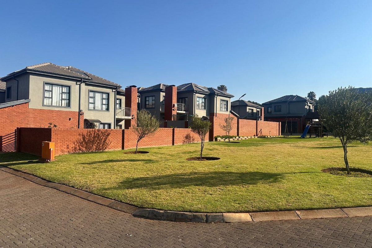 A view of the residential complex featuring well-maintained brick boundary walls, paved driveway, and landscaped communal garden areas.