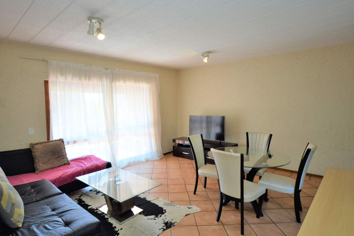 A living and dining area featuring tiled flooring, ceiling spotlights, and a sliding glass door providing natural light.