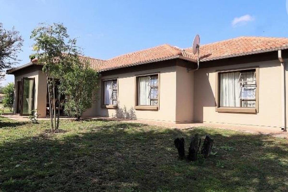 Rear view of a single-story house featuring a tiled roof, beige exterior walls, and large windows overlooking a garden area.