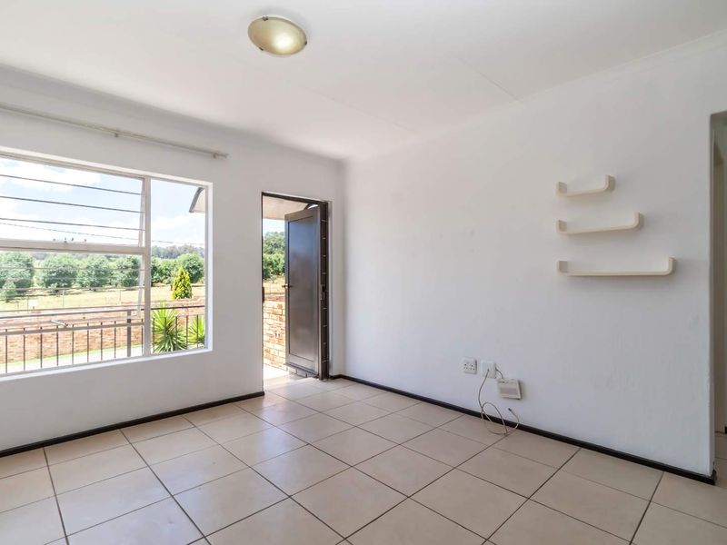 A bright, empty living room featuring neutral tiled flooring, a large window with natural light, and direct access to an outdoor area.