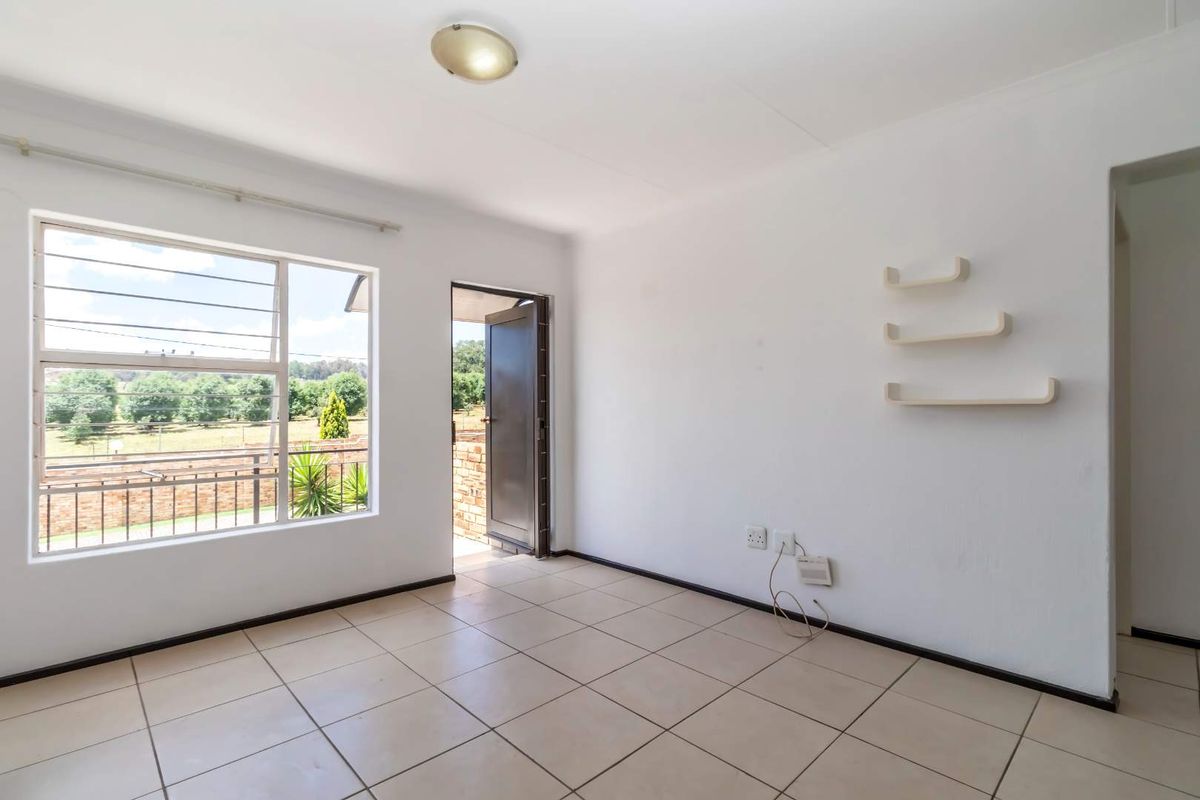 A bright, empty living room featuring neutral tiled flooring, a large window with natural light, and direct access to an outdoor area.