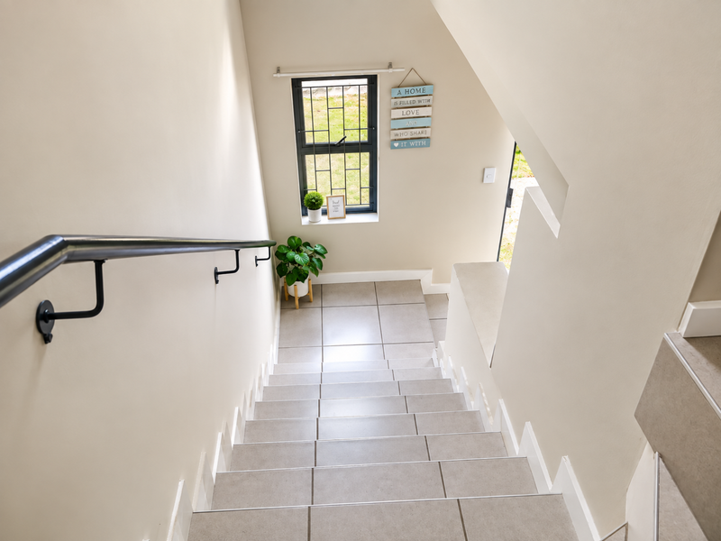 A bright, well-maintained staircase featuring neutral floor tiles, a modern metal handrail, and a leaded glass window providing natural light.